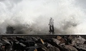 A man is drenched by a large wave during high tide as he cycles past at a fishing