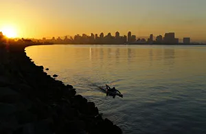 A man glides across the water on a paddle board as the sun rises in San Diego