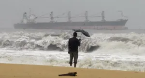 A man holding an umbrella watches large waves on the Marina beach as a cargo ship passes A man holding an umbrella watches large waves on the Marina beach as a cargo ship passes