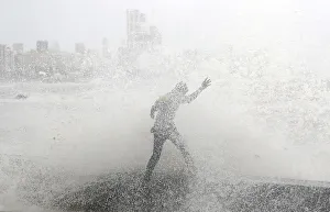 A man loses his balance as he gets drenched by a large wave during high tide at a A man loses his balance as he gets drenched by a large wave during high tide at a