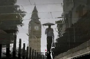United Kingdom Prints: A man is reflected next to Big Ben on a wet pavement during a rainy day in central London