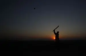 A man is silhouetted against the setting sun as he plays cricket at a park in Lahore