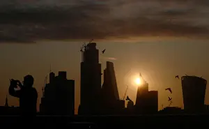 A man takes a photograph of the skyline as the sun rises behind the city of London