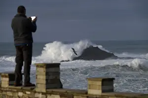 Spain Prints: A man takes pictures of waves as they crash against a lighthouse in the port town of
