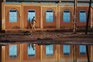 A man walking past a school is reflected in a large puddle in Niamey