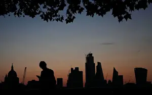 A man walks past the city of London financial district as dawn breaks in London