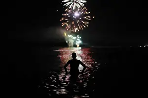 A man watches fireworks as he takes a bath in the Mediterranean Sea on San Juans night