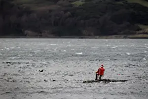 A mannequin dressed as a fisherman in a Santa costume sits on a rocky outcrop in