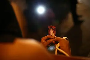 A masked penitent prays as he holds an image of Jesus Christ during a procession as part