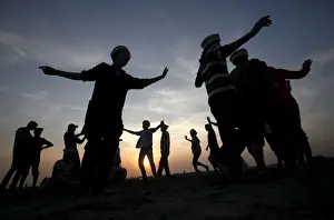 Men are silhouetted as they dance to celebrate during sunset at a beach in Karachi
