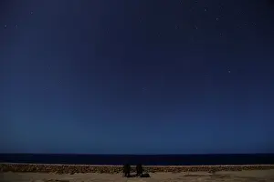 A meteor streaks past stars as people face the sea hoping to catch a glimpse of shooting