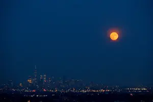 The full moon rises over the skyline of New York and One World Trade Center as seen