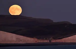United Kingdom Prints: The moon is seen rising behind the Seven Sisters Cliffs at Birling Gap in East Sussex