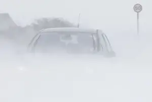 A motorist drives through snow blown from fields near Buxton in central England