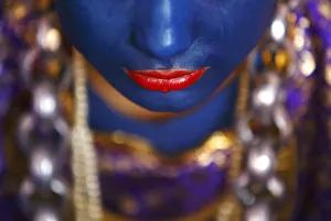 A Newari woman, with her lips and face painted to depic a deity, sits inside a house