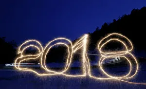 The numbers 2018 are written in the air with a sparkler on a roadside while cars drive The numbers 2018 are written in the air with a sparkler on a roadside while cars drive
