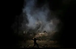 Palestinian demonstrator uses a sling to hurl stones at Israeli troops during a protest