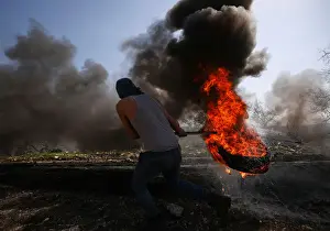 Prints of A Palestinian protester moves a burning tyre during clashes with Israeli troops following a protest against the nearby Jewish settlement of Qadomem Israel Prints: Palestinian protester moves a burning tyre during clashes with Israeli troops following a