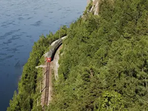 A passenger train moves along a railway along the bank of the Yenisei River near