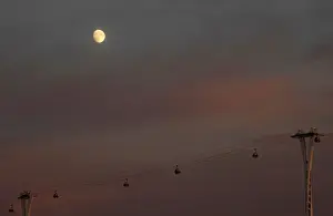 Passengers cross the River Thames in cable cars with the moon seen behind at dusk