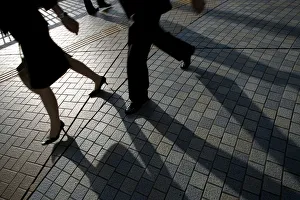 Pedestrians cast shadows as they walk on a street in Tokyo
