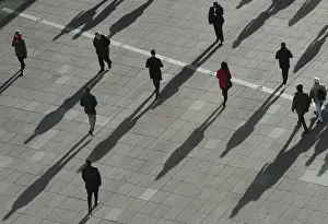 People cast long shadows in the winter sunlight as they walk across a plaza in