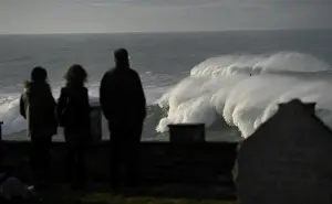 Spain Prints: People look at waves as they crash against a lighthouse in the port town of Tapia de