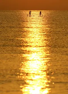People paddle on a stand-up board during sunrise in a beach in Larnaca