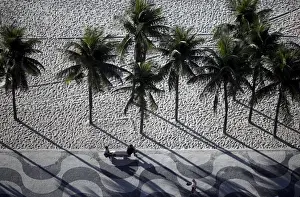 People sit on a bench on the sidewalk at Copacabana Beach in Rio de Janeiro, Brazil