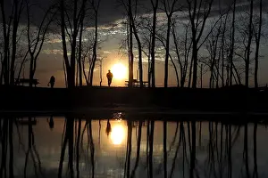People stand and watch the sun set as they are reflected in a puddle at Presque Isle