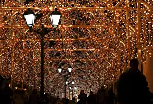 People walk along a street decorated with festive illumination lights, part of the New Year