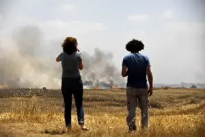 People watch a burning field, on the Israeli side of the border fence between Israel