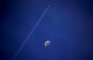 A plane leaves a vapor trail as it flies past the moon above the town of Gunnedah