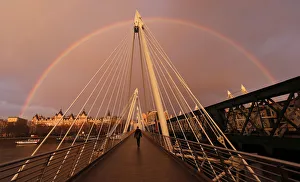 A rainbow appears as a pedestrian crosses one of the Golden Jubilee Bridges in London