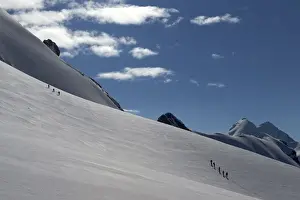 Roped parties of climbers walk on a glacier marking the border between Switzerland