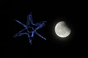 Prints of The shadow of the Earth falls across the face of the Moon, with a six-pointed decorative star on a Christmas tree in the foreground Russia Prints: The shadow of the Earth falls across the face of the Moon above Russias far eastern city