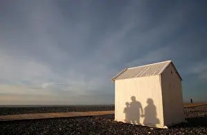 A shadow of a family is seen on a beach cabin on the pebbled beach during sunset in