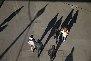 The shadows of pedestrians are cast on the pavement as they walk along the South Bank in