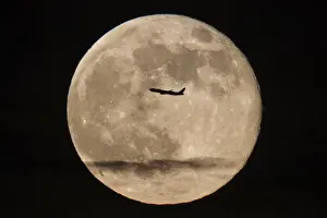 A silhouetted airplane flies past a super moon over New York