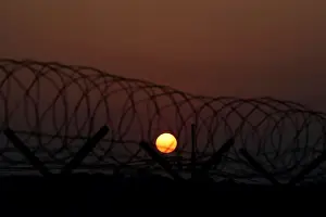 The sun rises over a barbed-wire fence at a checkpoint on the Grand Unification Bridge in