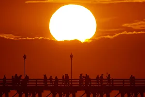 Images Dated 2018 July: The sun sets behind a cloud as people cool off with a walk along an ocean pier in