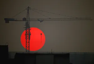 The sun sets behind a crane behind a construction site for a new residential building in The sun sets behind a crane behind a construction site for a new residential building in