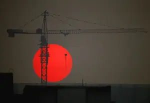 The sun sets behind a crane behind a construction site for a new residential building in