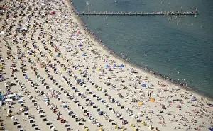 Sunbathers and roofed wicker beach chairs are seen along the beach on the bay of