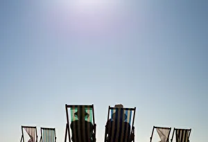 Sunbathers sit on deck chairs on Brighton beach, southern England