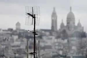 : A tv antenna is seen on the rooftops of residential buildings in front of the Sacre Coeur