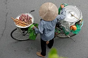 Vietnamese woman transports cooked cassava and potato for sale by a bicycle on a street