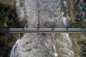 Environment Prints: A view shows vehicles driving along a bridge across the Mana River during an ice drift