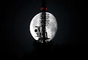 The waning gibbous moon shines behind a telecommunications tower in the Swiss mountain