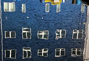 Windows take on different shapes as they reflect upon the water along a wharf in Portland